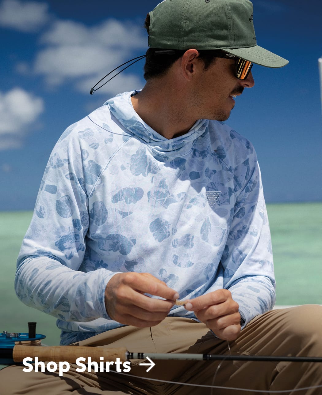 Man is tying a fly with a fishing rod on his lap. 