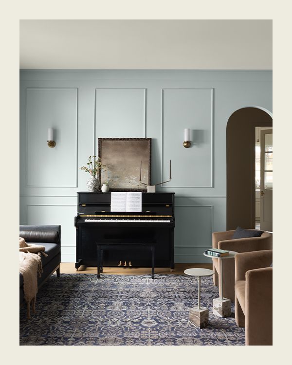 A pale blue painted living room with paneled walls, a decorative rug, and tan furnishings.