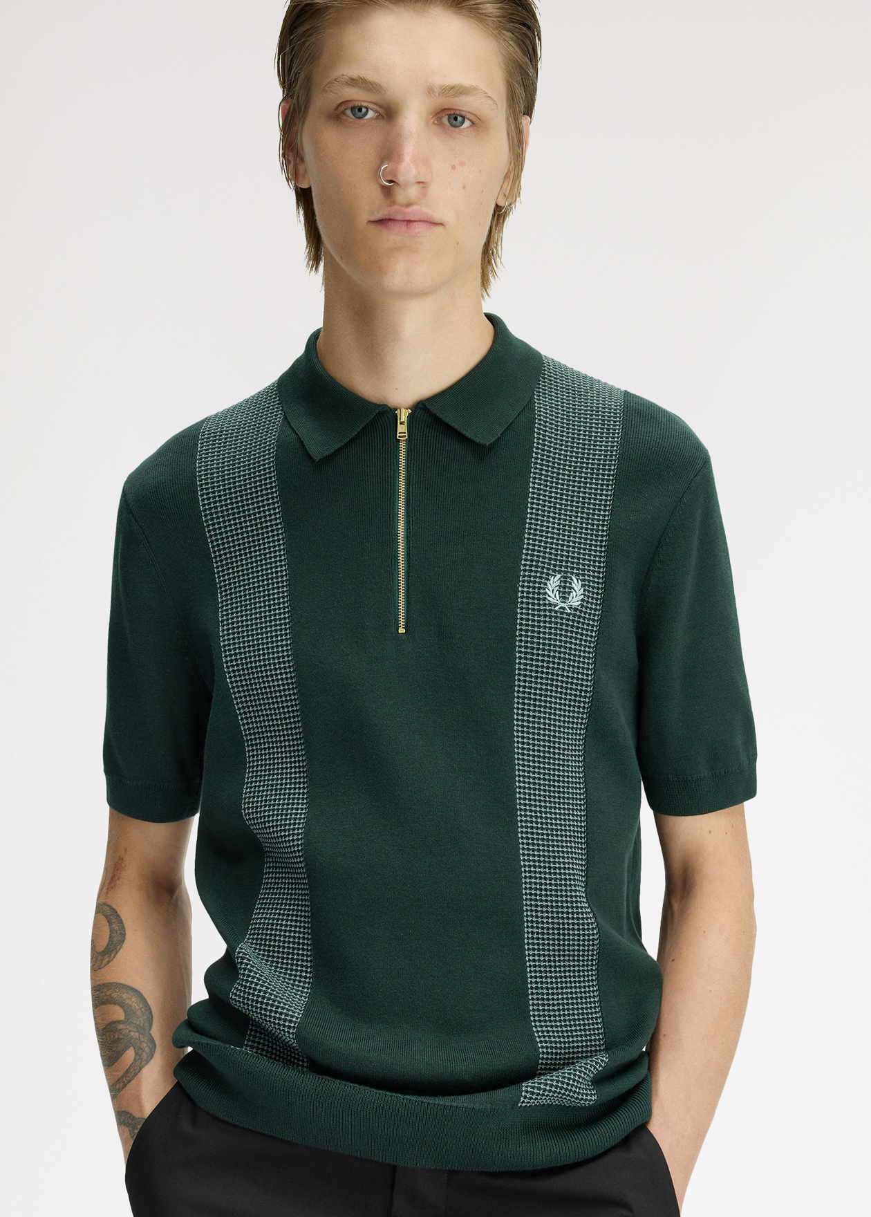 New Releases" Blonde male model looks into the camera with his hands in his pockets and wears a dark green zip knitted polo shirt with white and dark green waffle panelling on either side of his chest