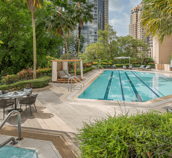 Urban pool area surrounded by lush greenery and tall buildings.