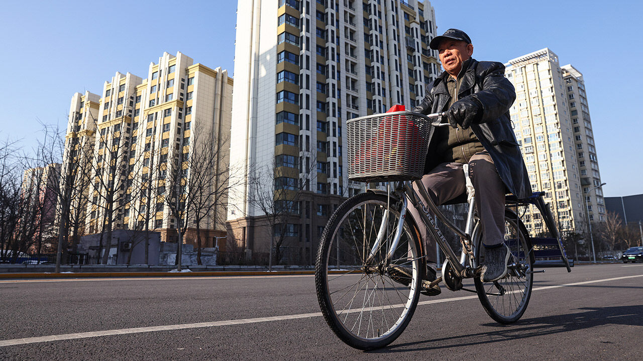 An elderly man rides a bike beside residential buildings in Beijing, China.