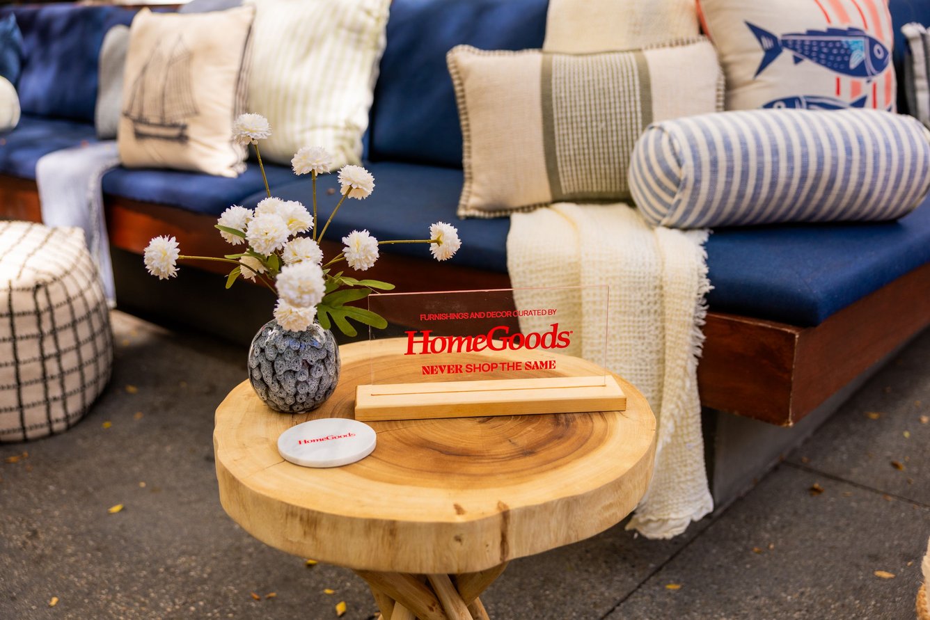 A clear HomeGoods sign sits on a table in front of a blue couch. 