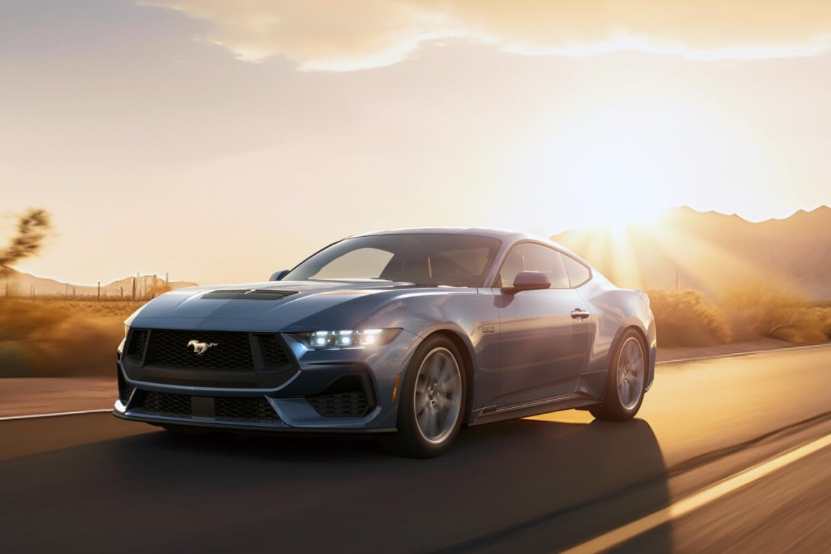 A 2024 Ford Mustang&reg; model being driven on a highway, sun setting in the background