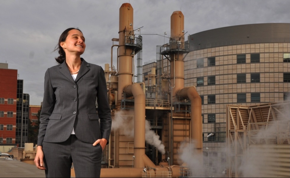 Nurit Katz, in gray pantsuit, with steam-generating equipment and buildings in background 