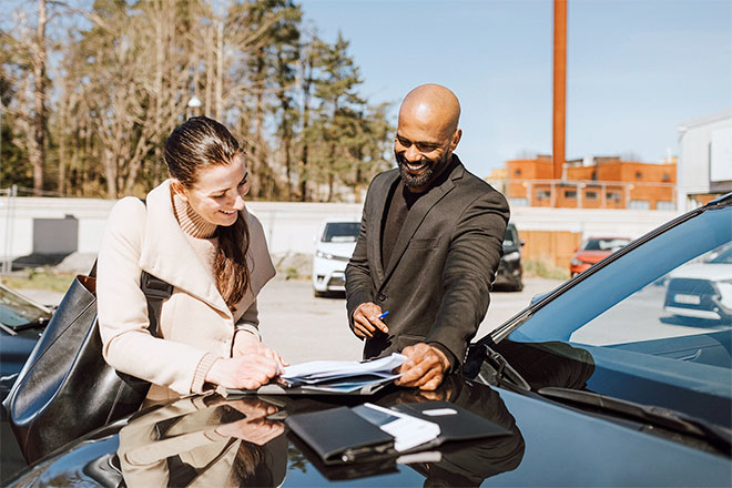 Two people signing forms on the hood of a car.