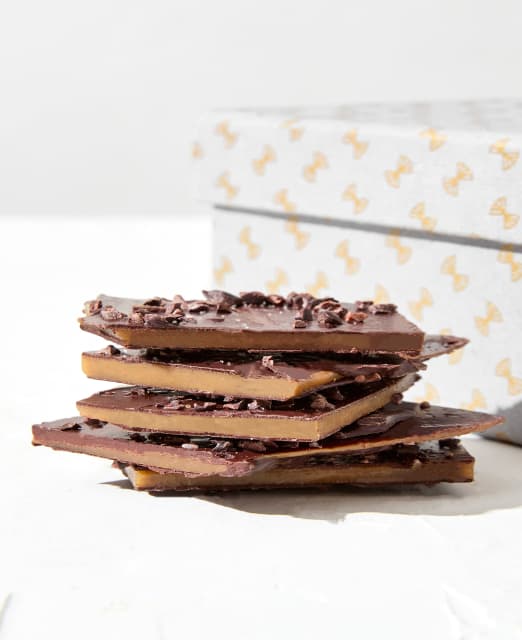 Stacked pieces of buttery toffee next to a beribboned box.