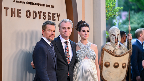 Three people pose in front of a sign reading 'The Odyssey'