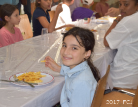 A young girl sitting at a table with a plate of food, smiling.