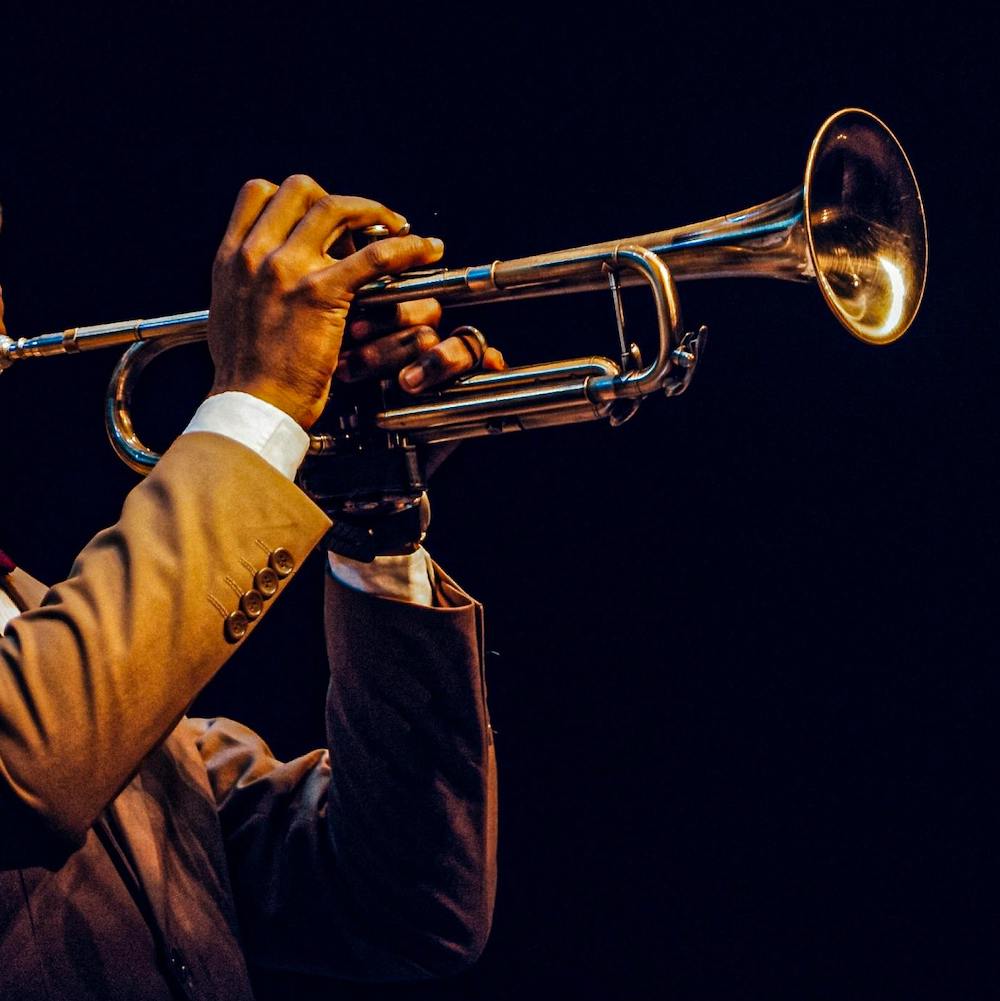 A close-up on a man's hands as he plays a trumpet under stage lights.