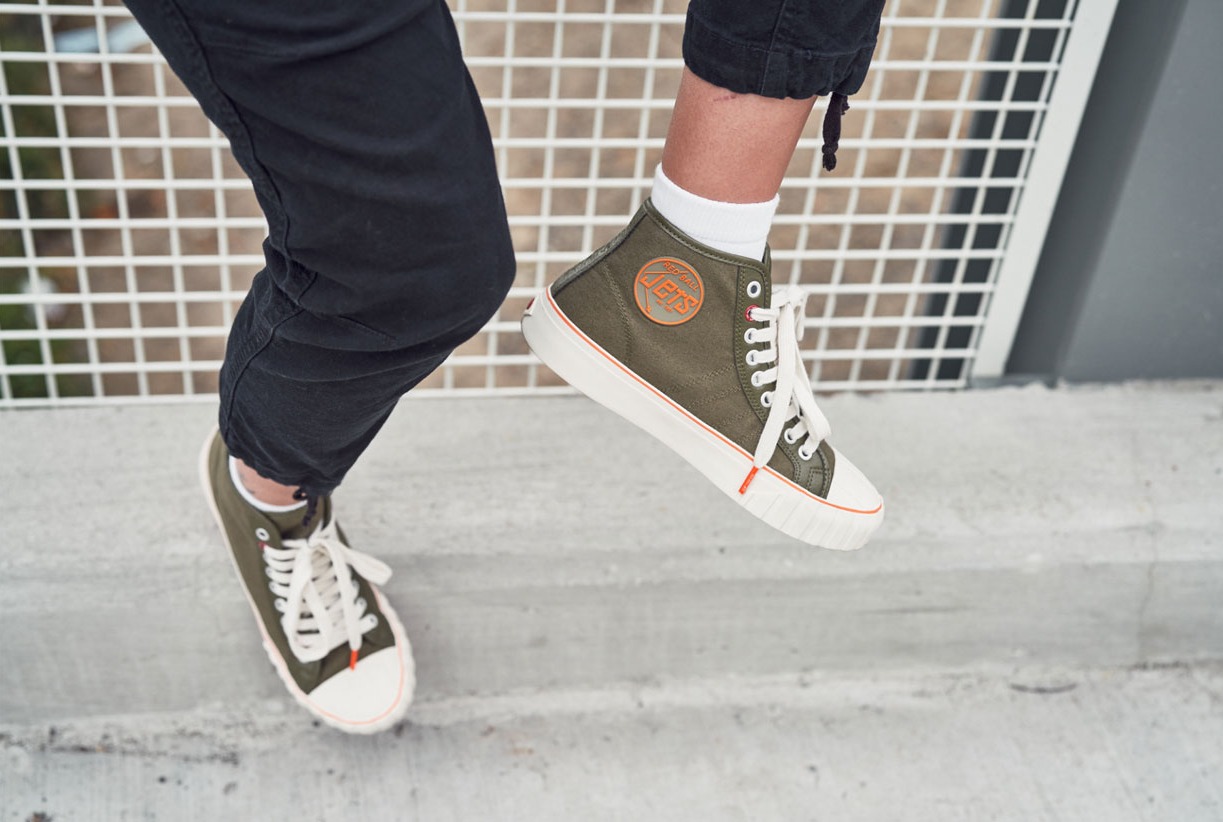 A person wearing the Olive '51 HI Red Ball Jets sits leaning on a metal railing on a concrete surface.