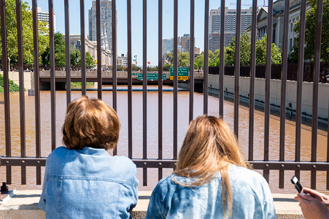Two people look through bars down at the flooded Schulkill River.