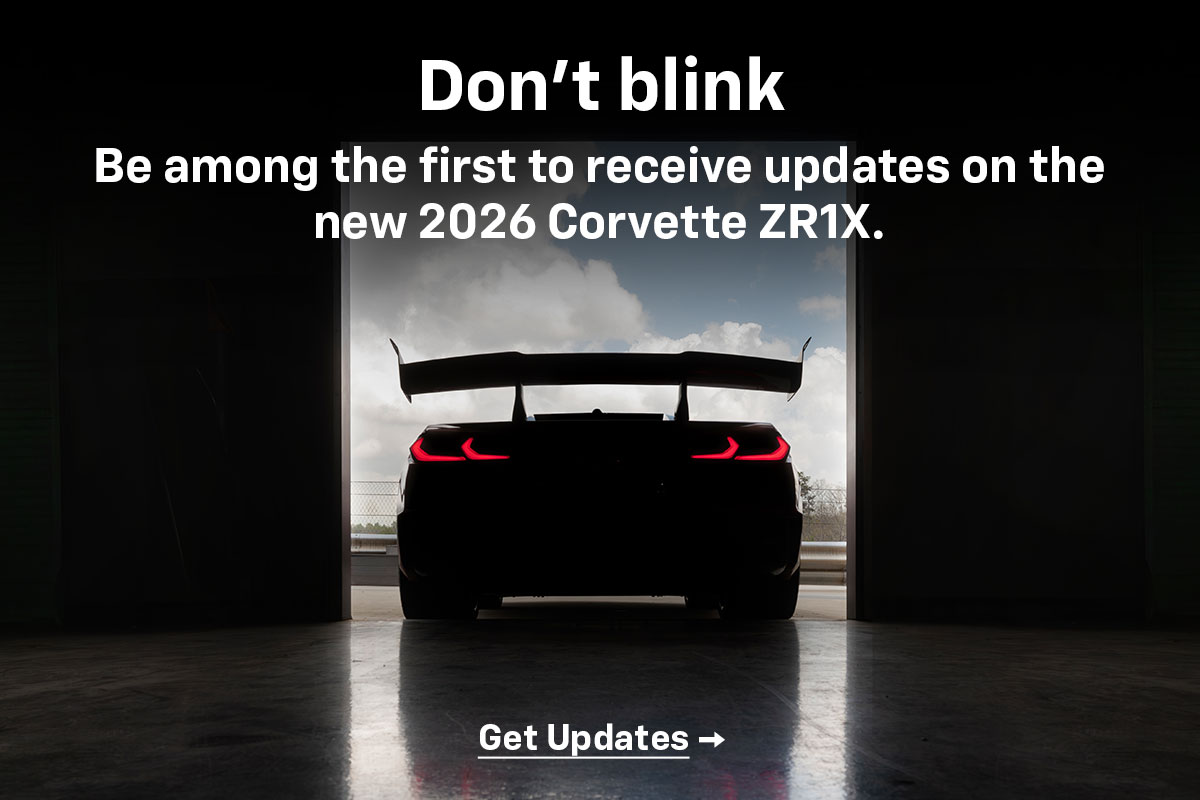 Rear shot of the ZR1X in shadow, tail lights glowing red, as it prepares to exit an open hangar bay door. Don't blink. Be among the first to receive updates on the new 2026 Corvette ZR1X. Get updates.