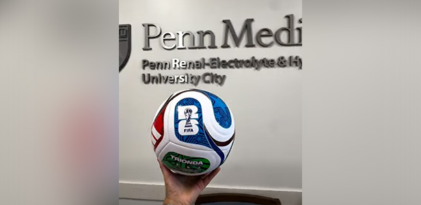 Hand holds soccer ball in front of Penn Medicine logo.