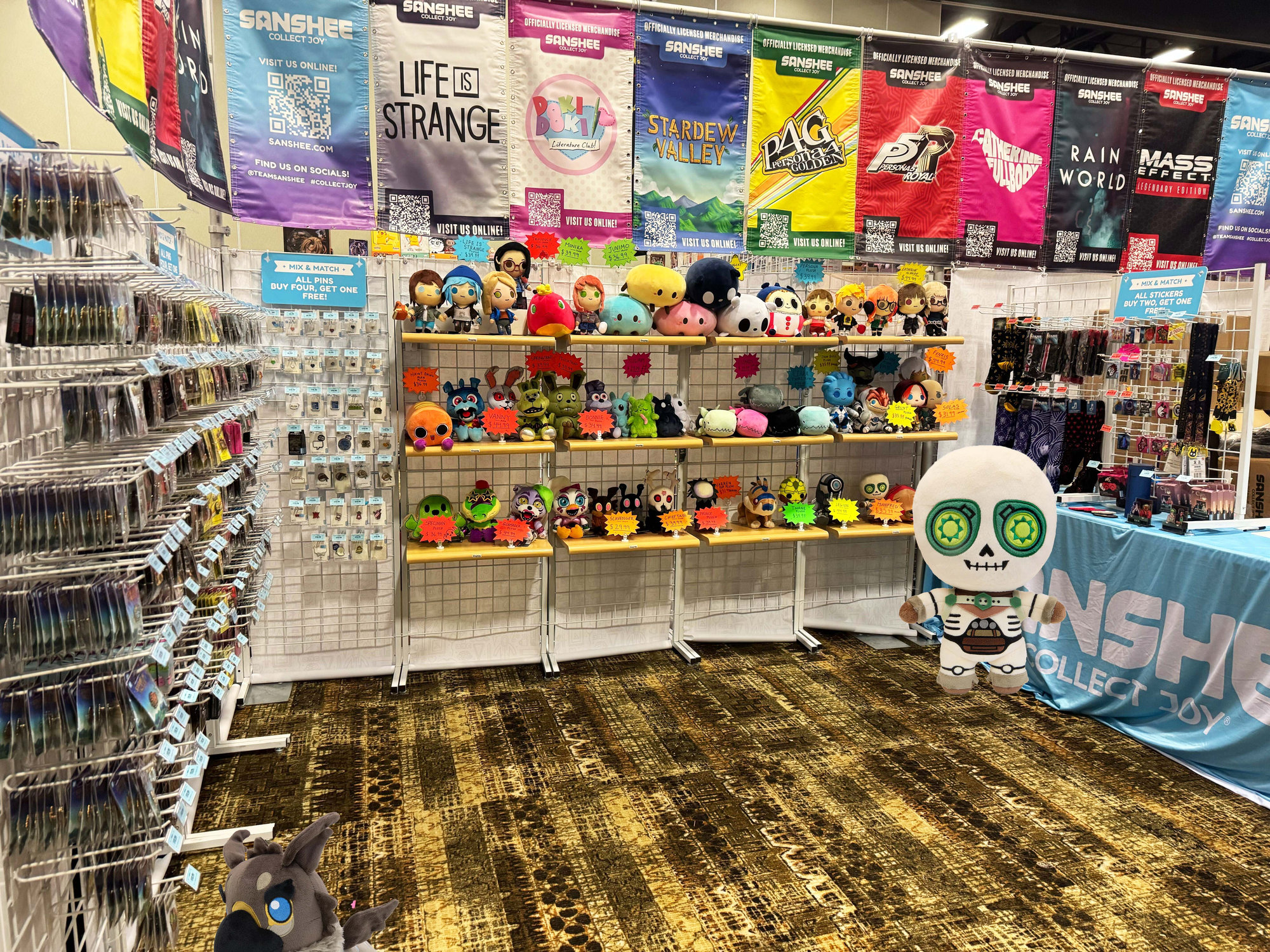 Manfred and Assan are hanging around the Sanshee booth at ColossalCon. Manfred is near the booth itself and Assan is at the bottom left.