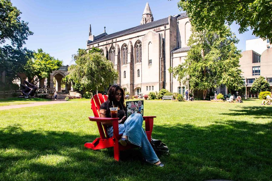 Photo: A BU student sitting in a red lawn chair on BU campus green space.