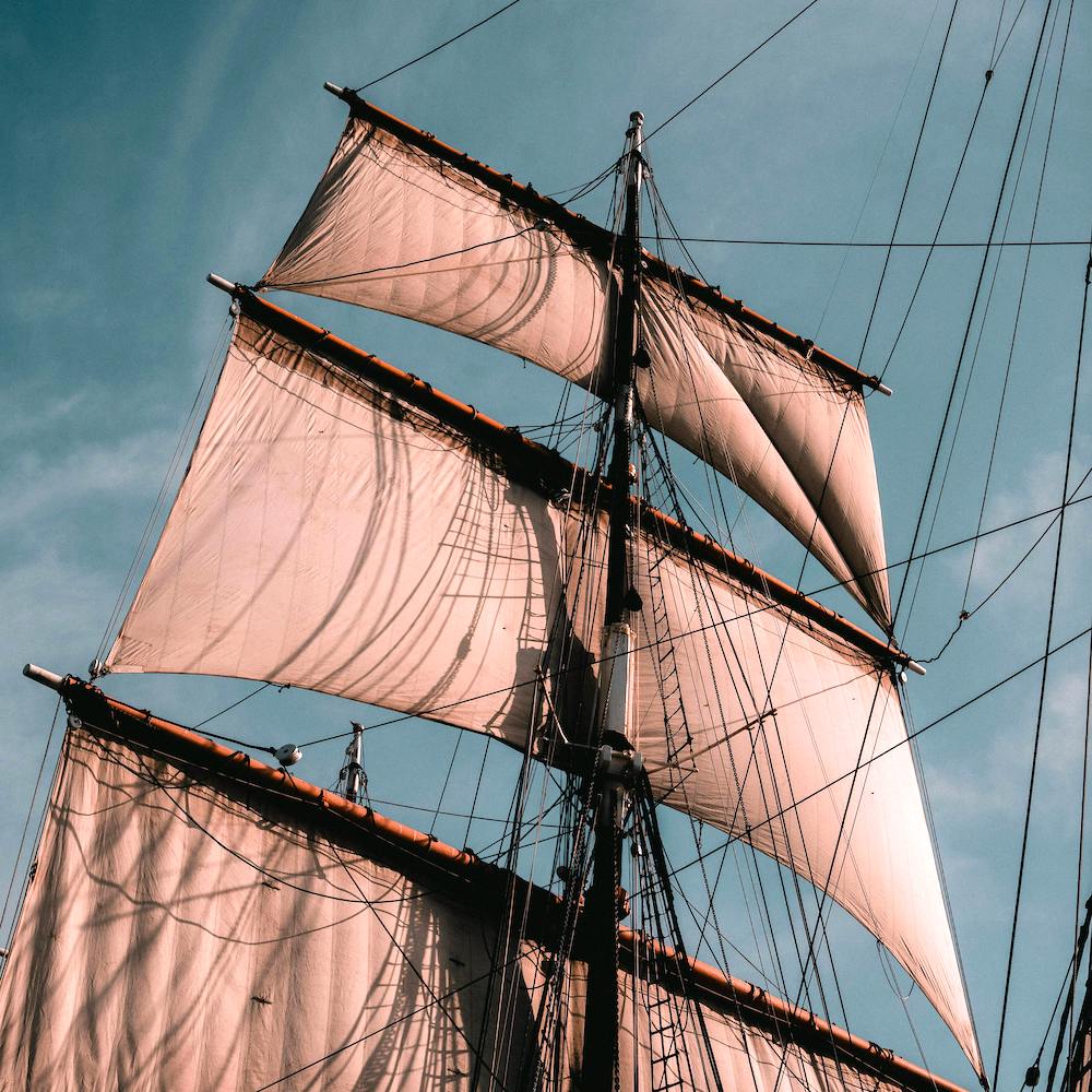 The rigging and sails of a tall ship, framed against a blue sky. 