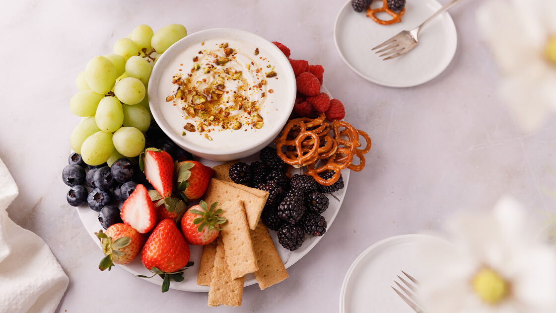 Close-up overhead image of dip arranged on a plate with a medley of fruit and pretzels.
