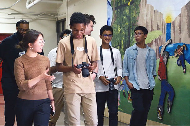 Ejun Mary Hong and Jack Nicholas Roney walk past a mural leading a group of students holding cameras.