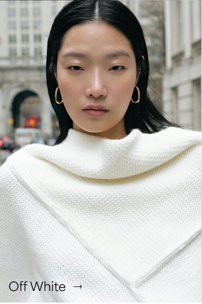 A close-up of Xun outdoors wearing The Palmer Long Sleeve Top with folded neckline details and gold hoop earrings, labeled “Off White”