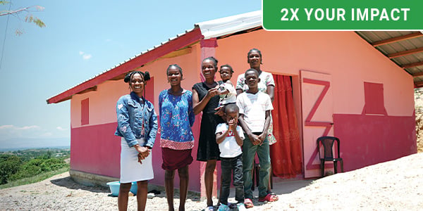 A family smiles in front of their safe, concrete home. 