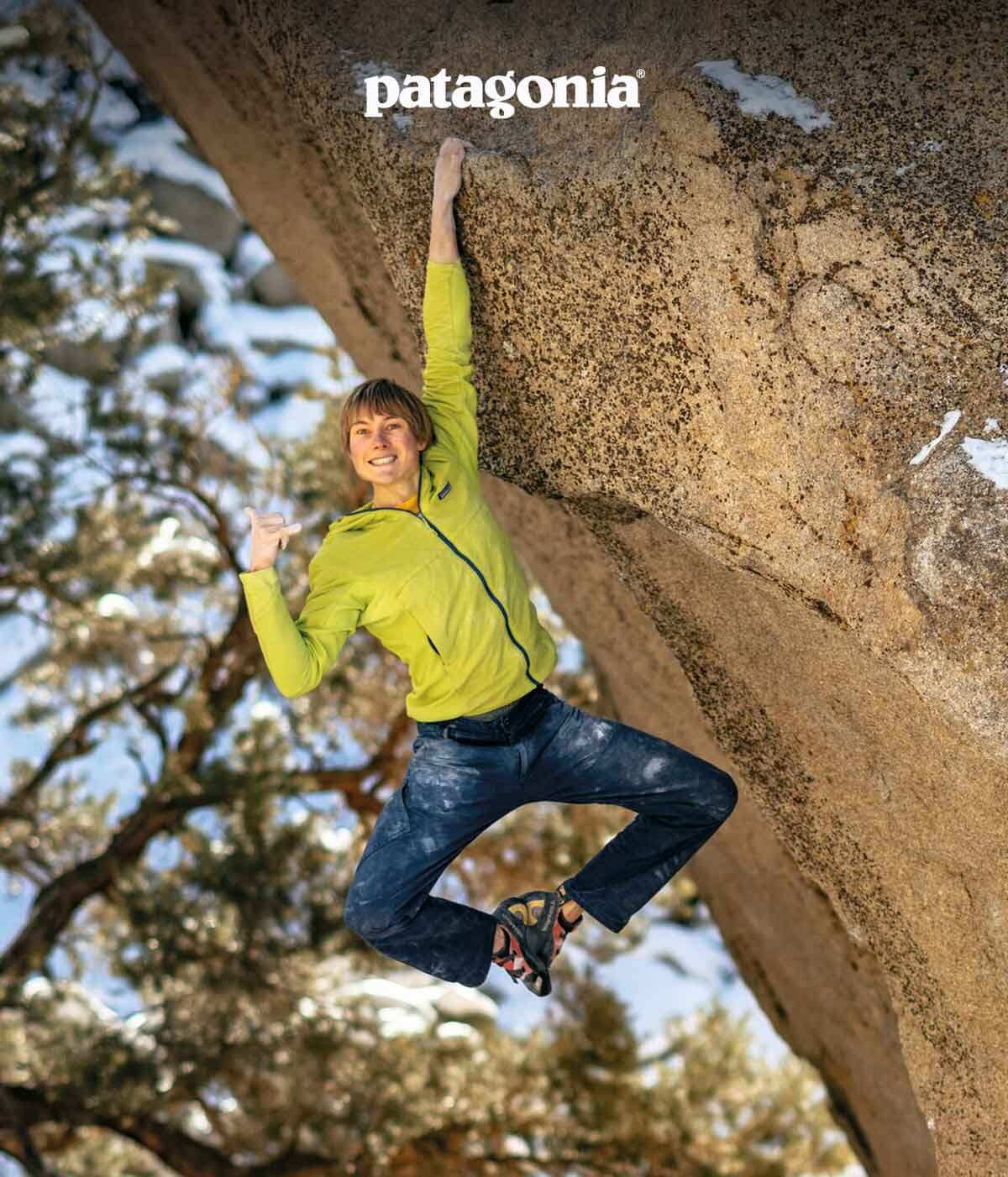 A climber smiles at the camera while hanging from a hold with one hand.