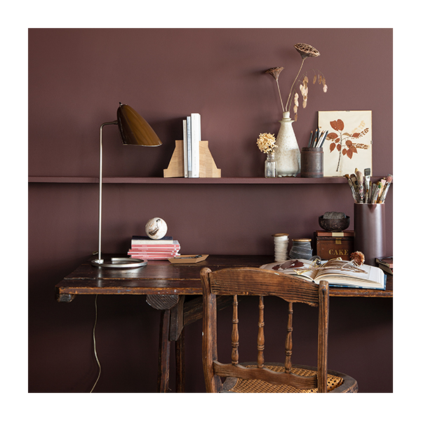 An office with brown-painted walls, a long wooden shelf, and a matching wooden desk and chair with various decorations.