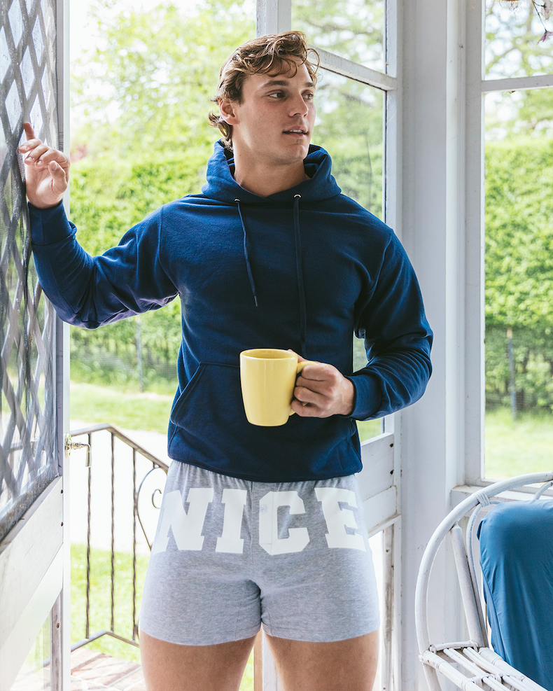 Man standing in doorway wearing navy blue sweatshirt and grey slim fit boxers with word NICE on the front.