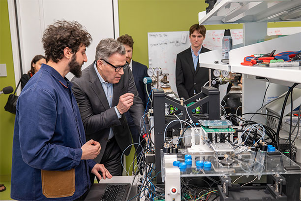Senator Dave McCormick (second from left) and Andrew Hanna (left) observing Hanna’s robotic system for rapidly formulating large numbers of lipid nanoparticles. (Image: Sylvia Zhang)