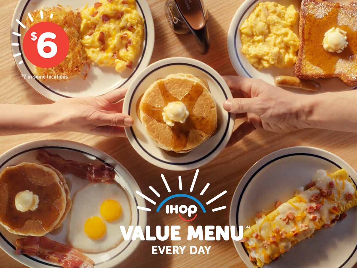 Two hands reach across a table to hold a plate of pancakes above Value Menu items on the table below