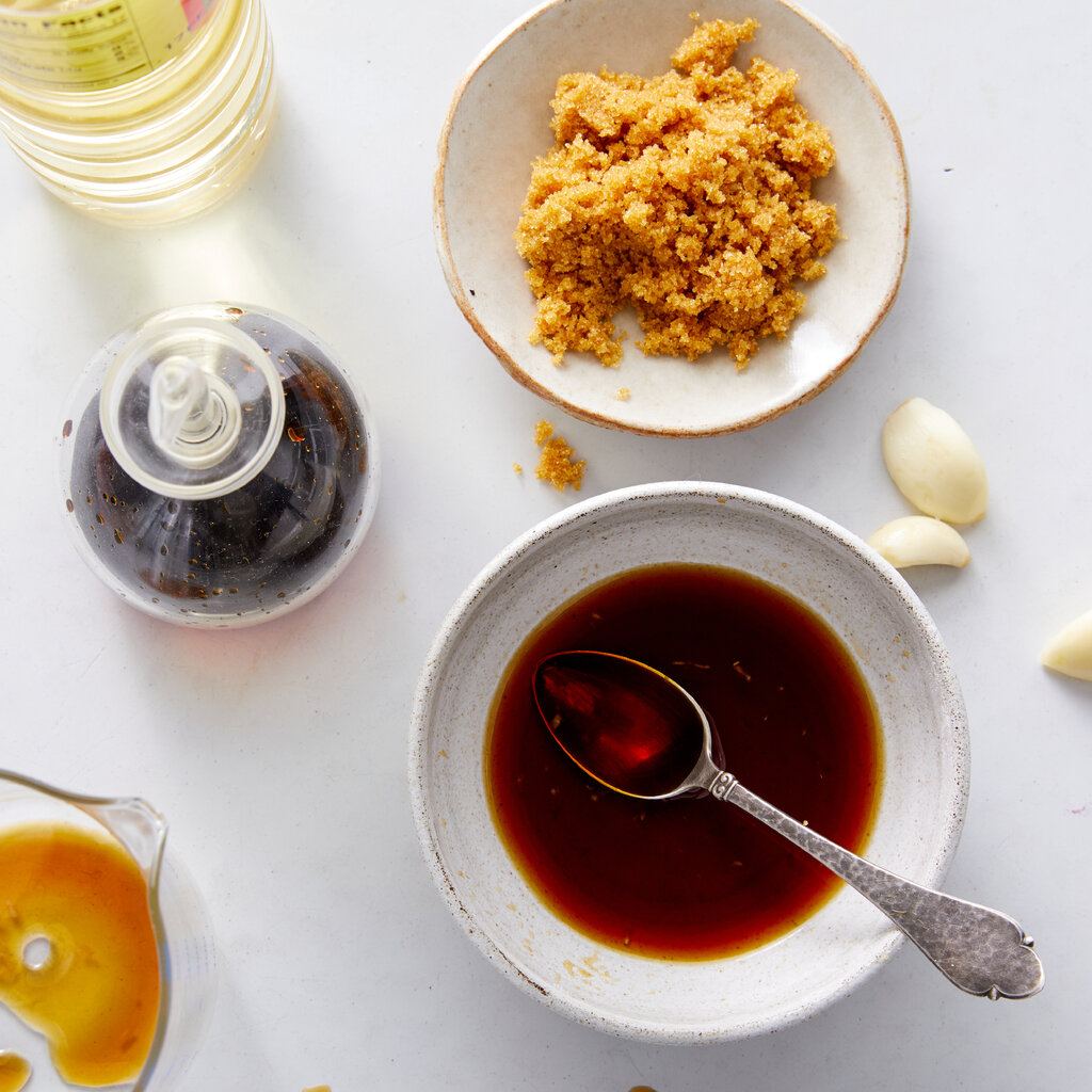 A bowl of teriyaki sauce is next to a bowl of brown sugar. 