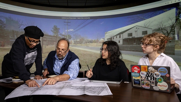 four people sit at table and look at maps
