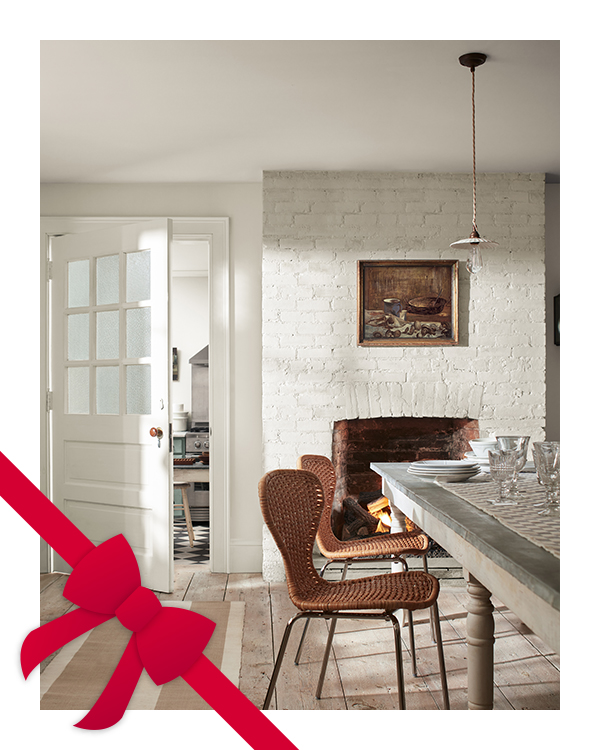 A white painted dining room houses a stone fireplace, a gray stone table, and brown woven chairs.