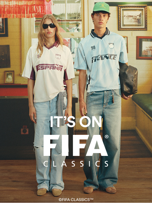 It's On FIFA Classics. Two models wearing vintage FIFA soccer jerseys with jeans in a retro interior setting.