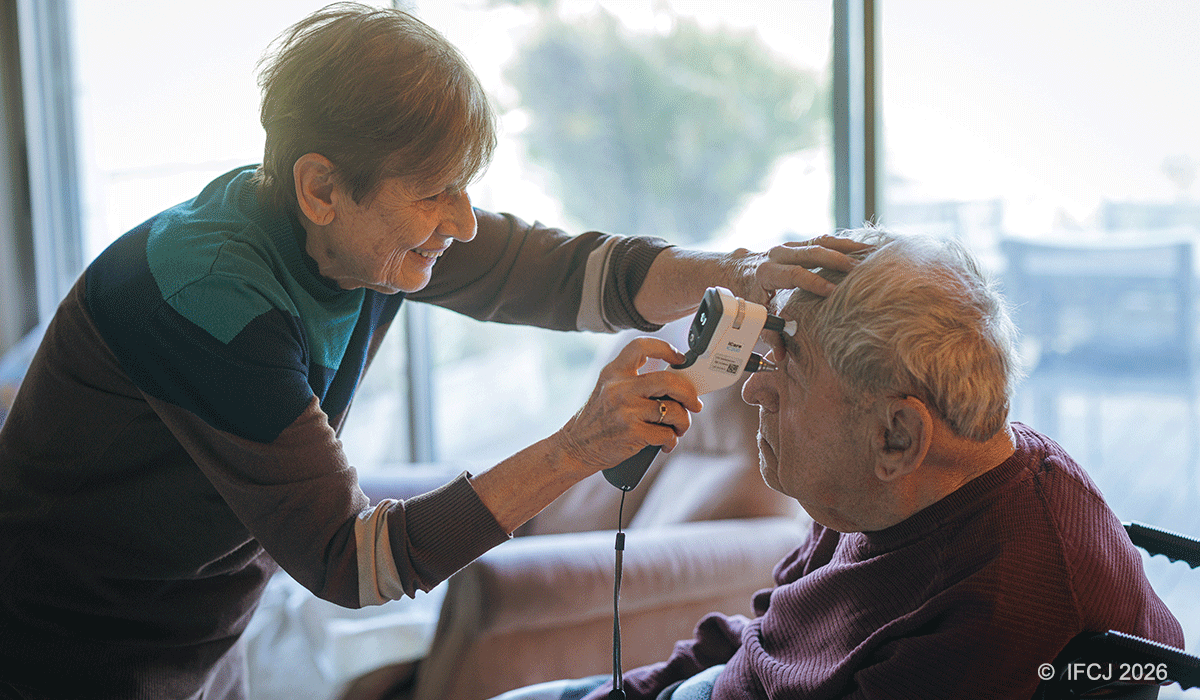 A woman using a device to check the eyes of an elderly man in a wheelchair.