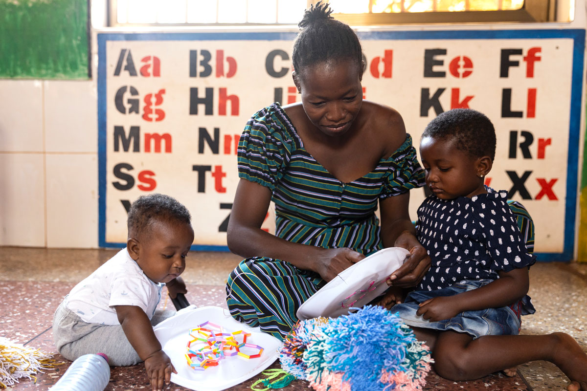 Mother sits next to her children, making toys out of household items.
