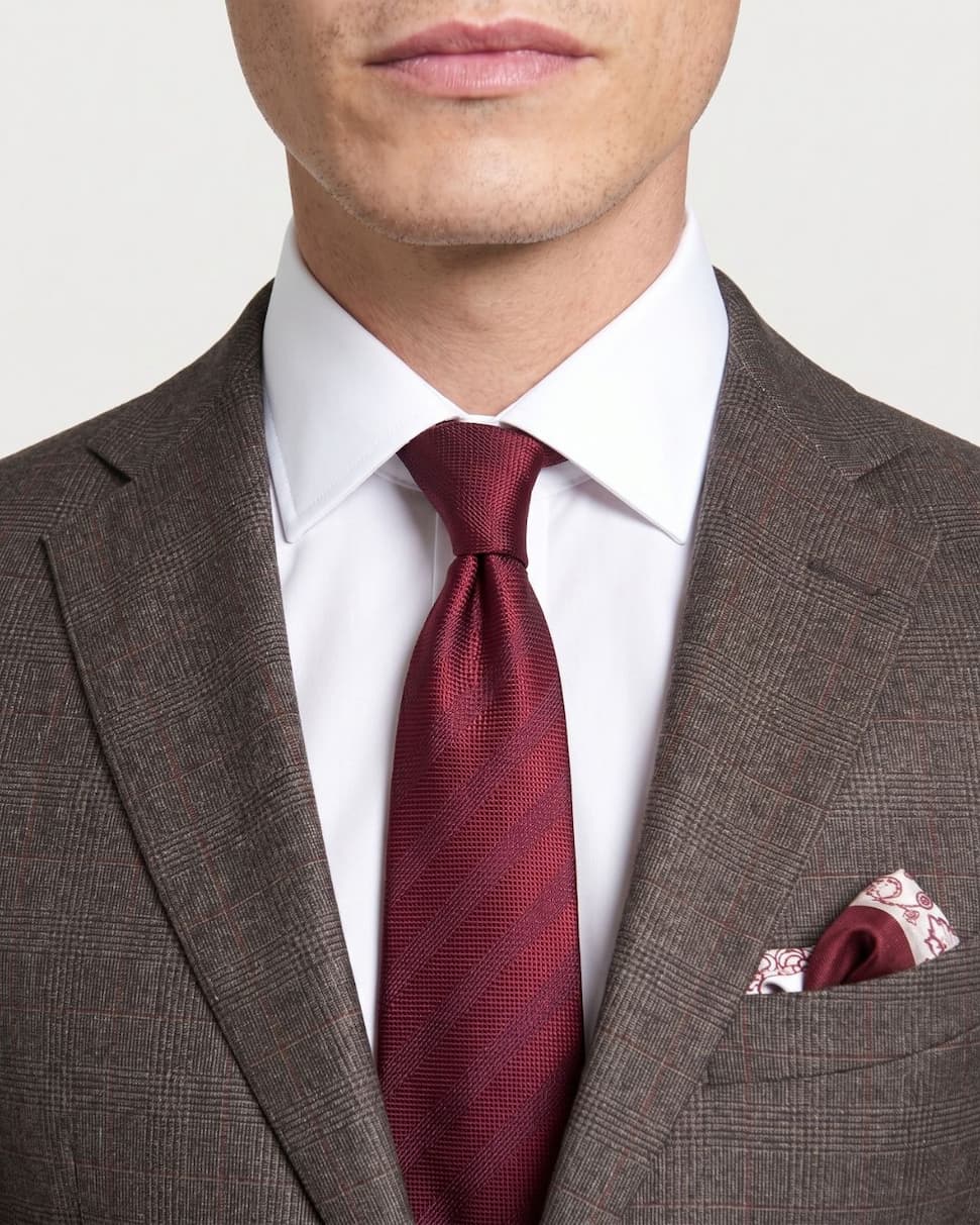 Man in a grey suit and pink tie adjusts his tie outdoors with guests in the background.