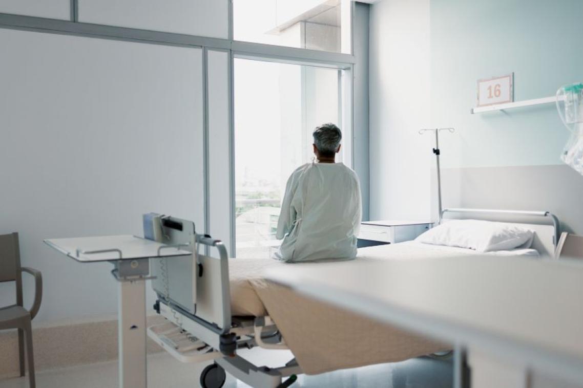 Man sitting on hospital bed with back to camera looking out window.
