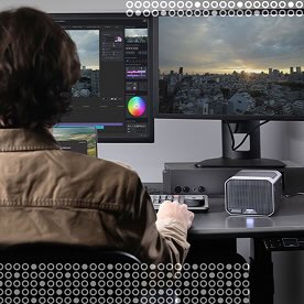 Person from behind editing video on a dual-monitor setup, with a city skyline displayed on one screen.