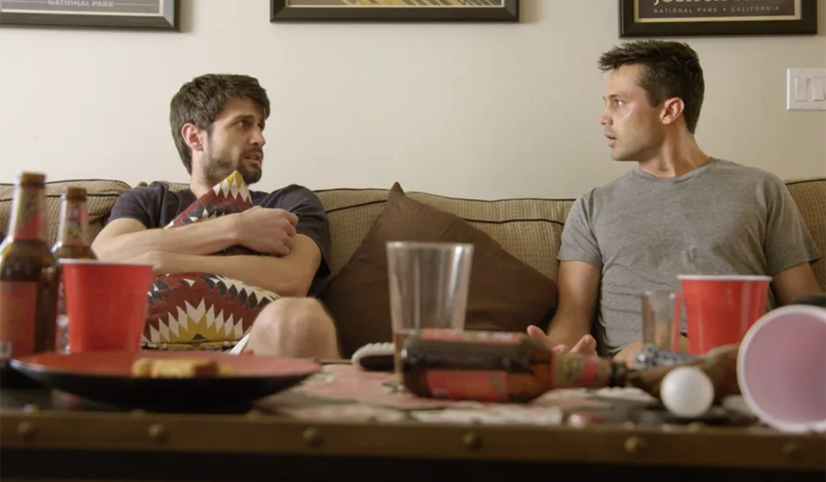 Two guys sitting on a sofa with beer bottles on the coffee table.