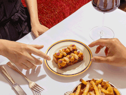 An animated image in which two people’s hands raise rectangular toasts topped with uni and perform a toasting motion.