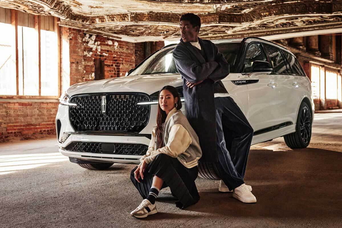 A stylish man and woman posing in front of a white 2025 Lincoln Aviator&reg; Reserve model parked in an old theater.