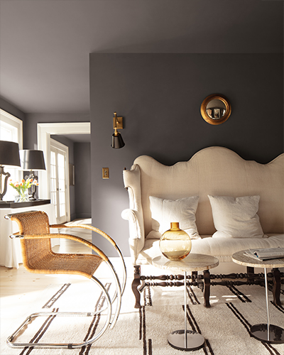 A rich chocolate brown living room featuring a tufted cream sofa and a rattan seat set on a white area rug with black stripes.