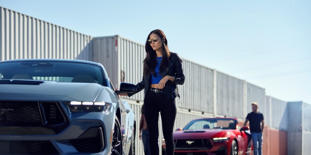 A woman standing beside a blue Ford Mustang&reg; model, and a man standing beside a red Mustang convertible