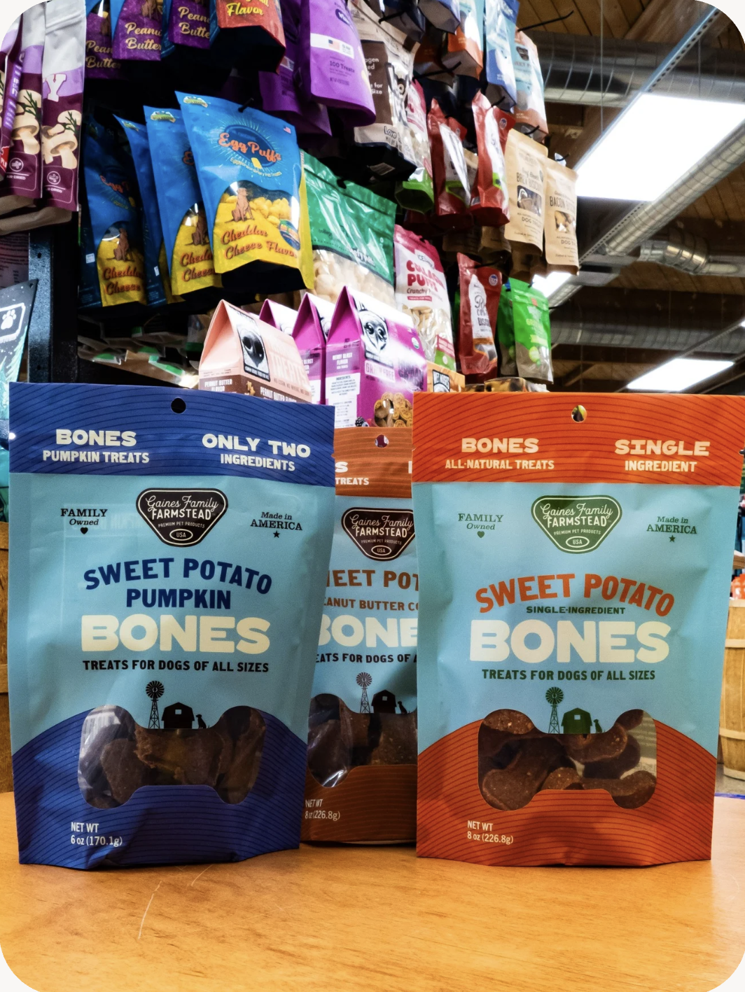 Photo of 3 bag varieties of the Gaines Family Farmstead Sweet Potato Bones inside a Mud Bay location. Photo shows the regular Sweet Potato Bones, Sweet Potato & Pumpkin and the Sweet Potato and Peanut Butter options in the 8oz bags.