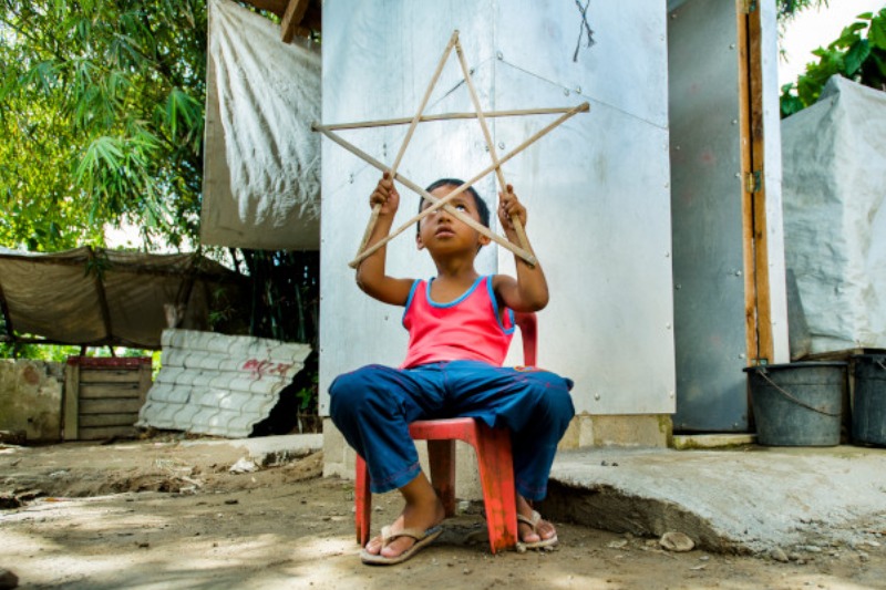 A child sitting on a red chair holding a wooden star frame.