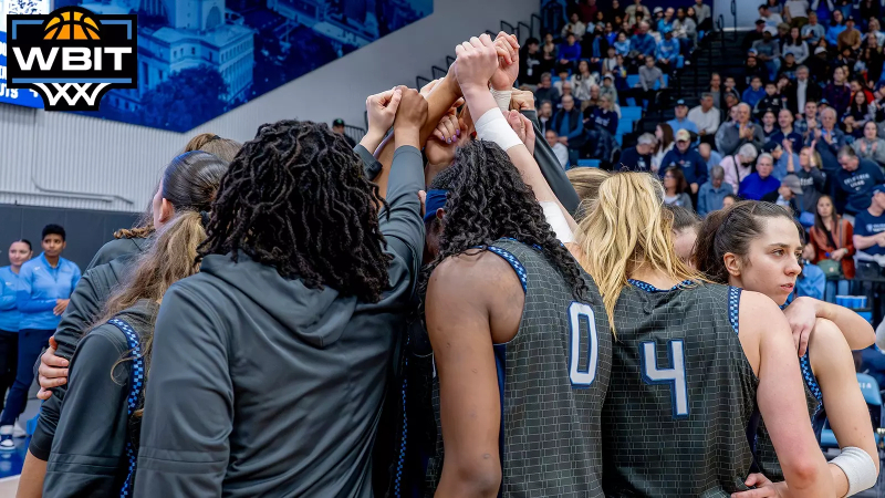 Columbia Women's Basketball players stand in a huddle in Levien Gymnaisum. The WBIT logo is in the top left corner.  Photo by: Columbia University Athletics / Stockton Photo, Inc.