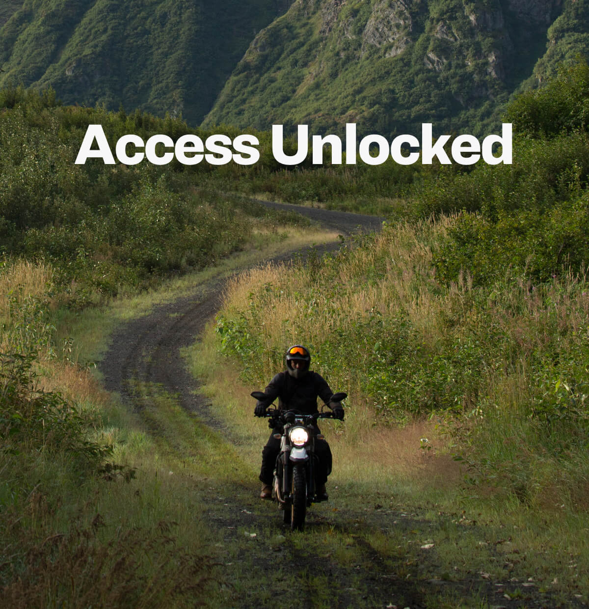 photo of a man riding a motorcycle through a grassy, wild path and the words access unlocked