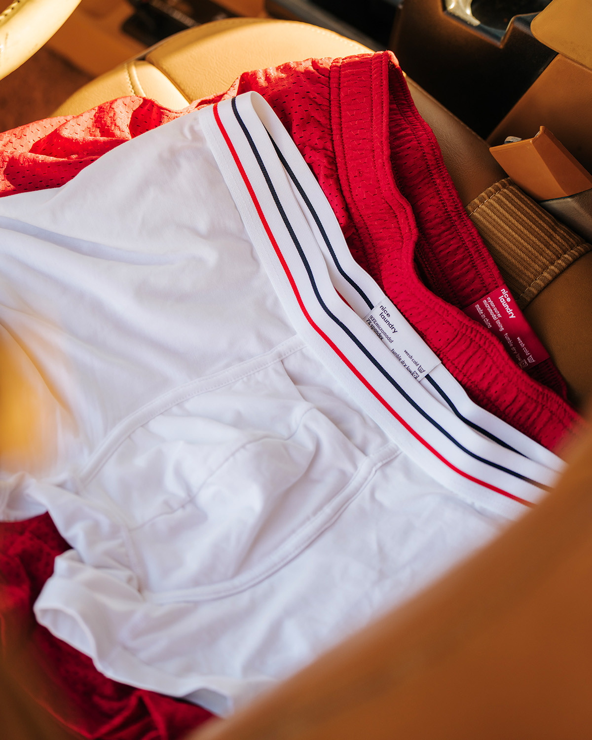 A pair of white boxer briefs with red/white/blue waistband sitting on red lounge shorts inside of a car.