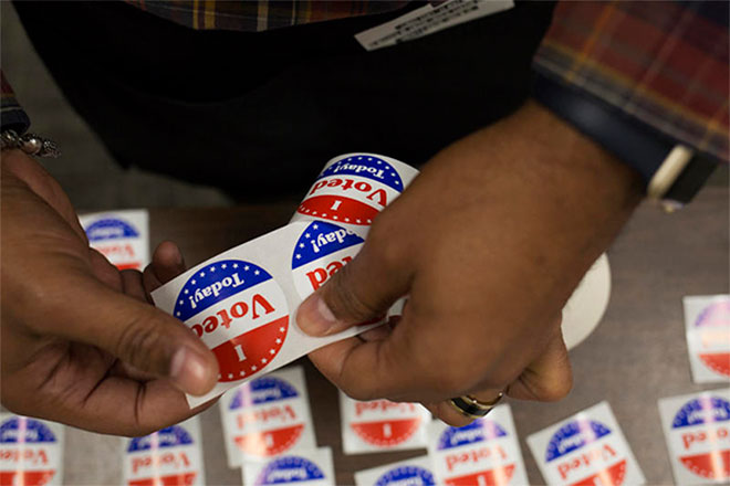 A hand peels off "I Voted Today" stickers.