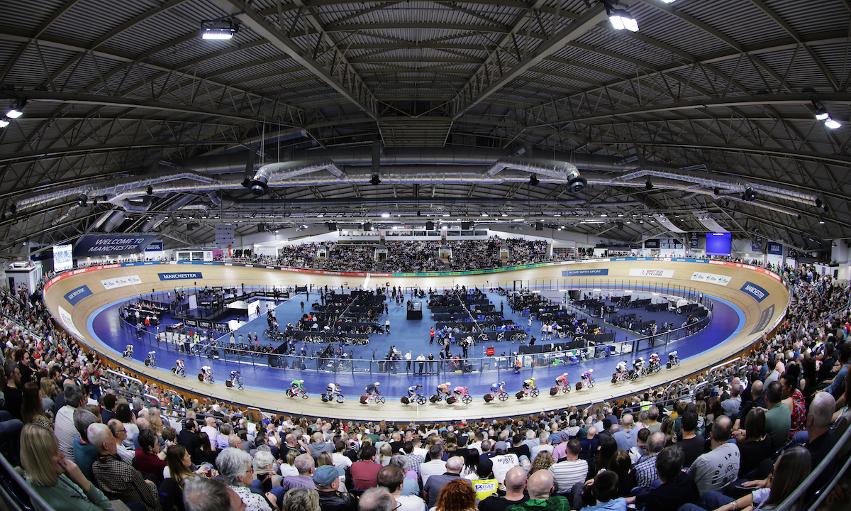 A wide-angle image of the Manchester velodrome during the 2025 Lloyds National Track Championships, showing a sold out crowd watching riders race.